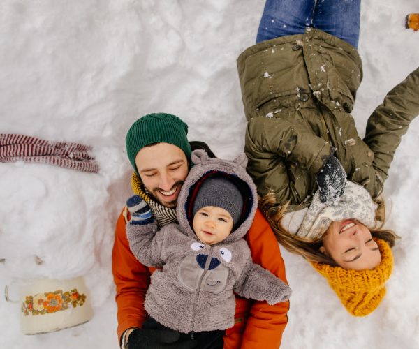 Ritratto di un bambino e dei suoi genitori orgogliosamente in posa con un pupazzo di neve che hanno fatto insieme