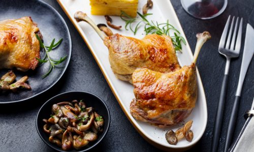 Duck legs confit with potato gratin and mushroom on a plate. Close up.